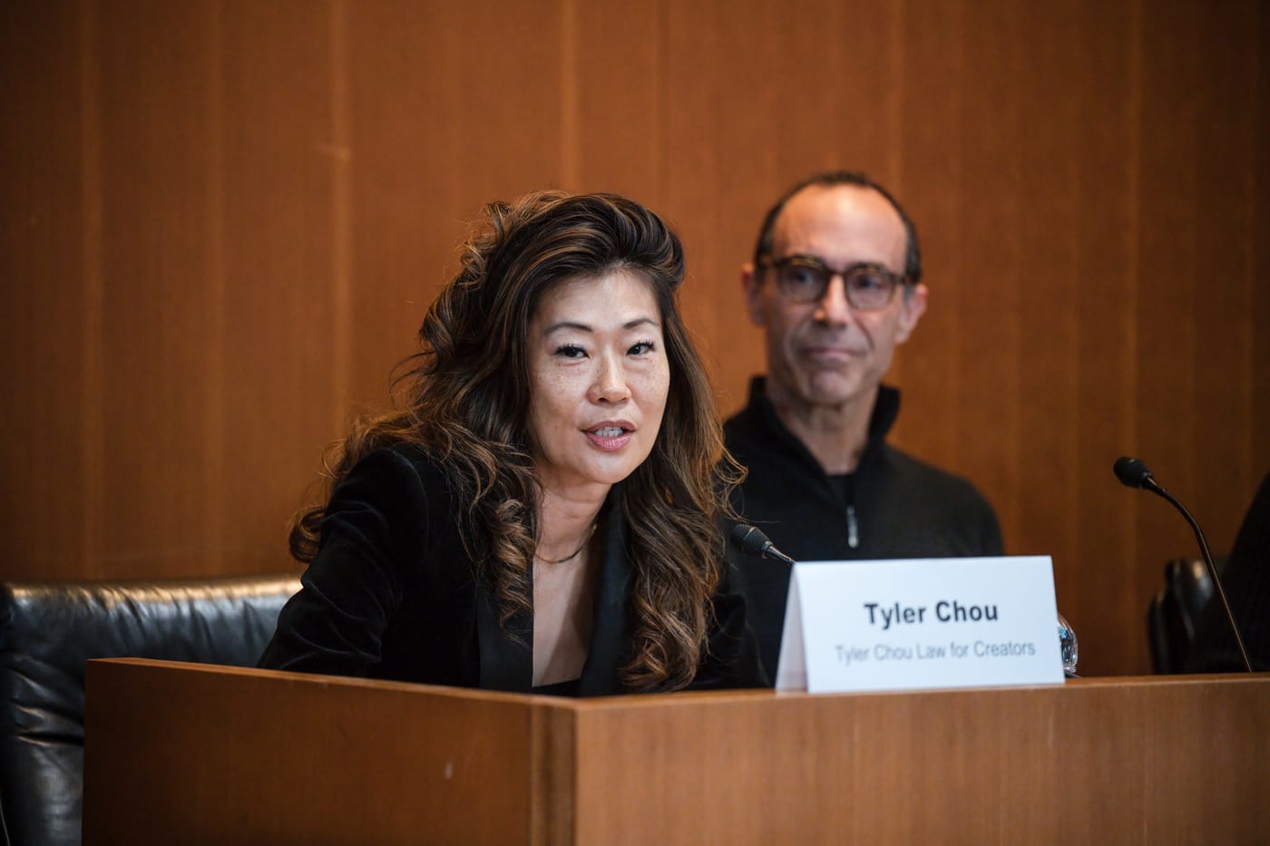 Tyler Chou speaking from the panel table at the Loyola Law School Power Players Symposium, behind a nameplate reading Tyler Chou, Tyler Chou Law for Creators.